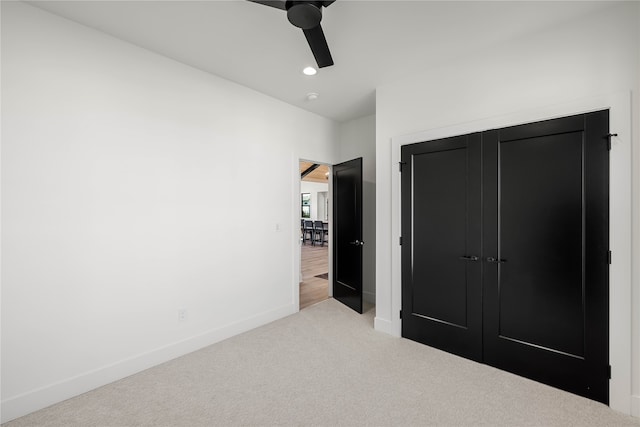 unfurnished bedroom with a closet, light colored carpet, and ceiling fan