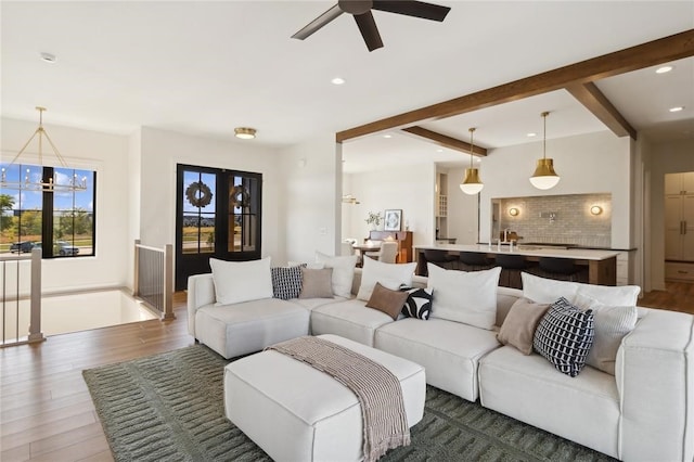 living room with dark wood-type flooring, beamed ceiling, and ceiling fan with notable chandelier