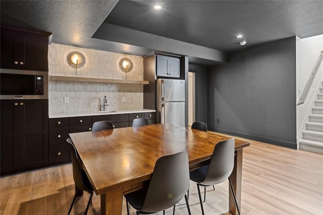 kitchen with backsplash, appliances with stainless steel finishes, a textured ceiling, light hardwood / wood-style flooring, and sink