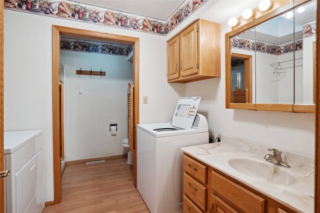 clothes washing area with sink, light hardwood / wood-style flooring, and washing machine and clothes dryer