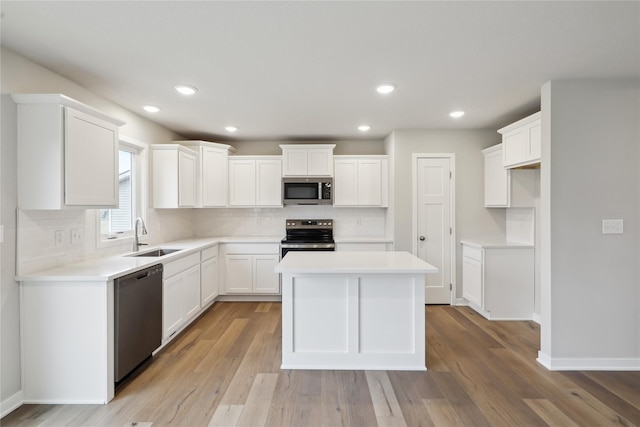 kitchen featuring light wood finished floors, appliances with stainless steel finishes, a center island, white cabinetry, and a sink