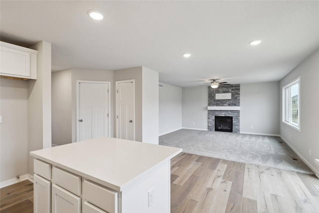 kitchen featuring ceiling fan, a fireplace, a kitchen island, white cabinetry, and light wood-type flooring