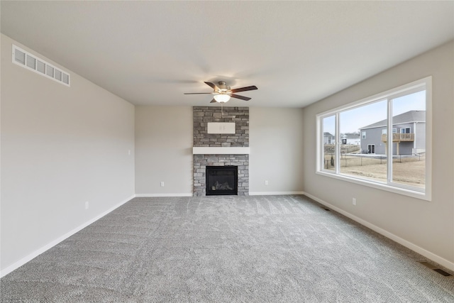 unfurnished living room with baseboards, visible vents, a stone fireplace, and carpet flooring