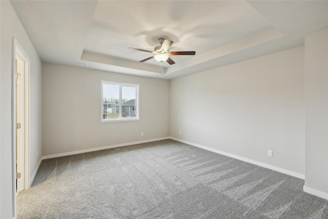 carpeted empty room with baseboards, a raised ceiling, and a ceiling fan