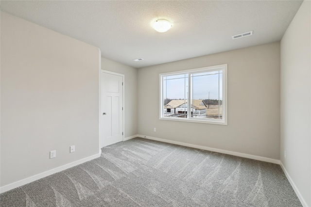 spare room with a textured ceiling, carpet flooring, visible vents, and baseboards