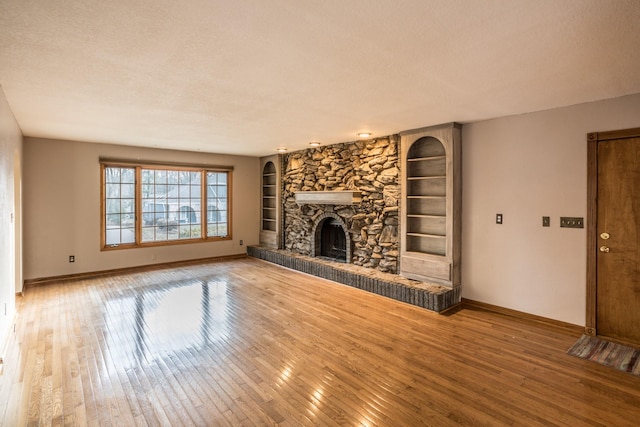 unfurnished living room featuring a stone fireplace, built in shelves, a textured ceiling, and hardwood / wood-style flooring