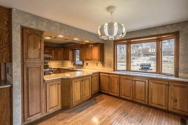 kitchen with pendant lighting, wood-type flooring, a chandelier, kitchen peninsula, and stainless steel range with gas stovetop