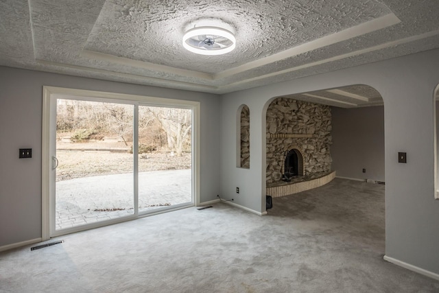 unfurnished living room with a stone fireplace, a raised ceiling, carpet, and a textured ceiling