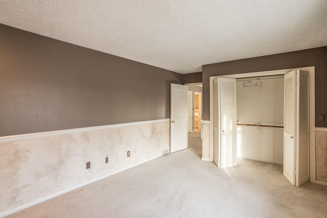 unfurnished bedroom featuring light colored carpet, a textured ceiling, and a closet