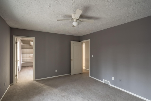 unfurnished bedroom with ceiling fan, a walk in closet, carpet floors, and a textured ceiling