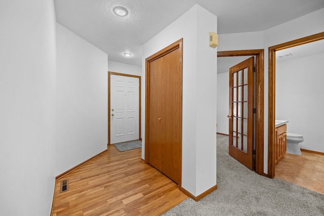 hall with a textured ceiling and light wood-type flooring