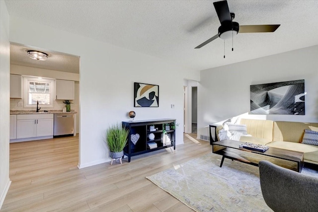 living room featuring a textured ceiling, ceiling fan, sink, and light hardwood / wood-style flooring