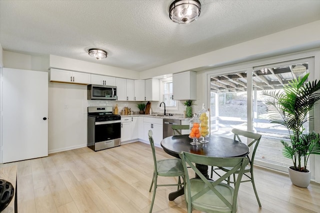 kitchen with sink, appliances with stainless steel finishes, a textured ceiling, white cabinets, and light wood-type flooring