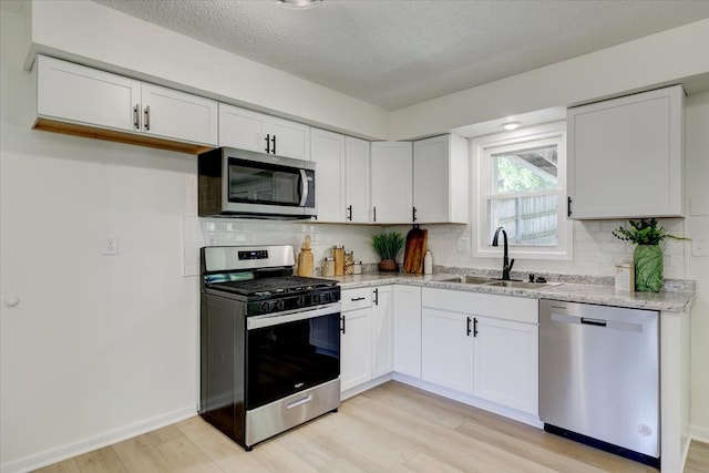 kitchen featuring light stone countertops, white cabinetry, sink, stainless steel appliances, and a textured ceiling