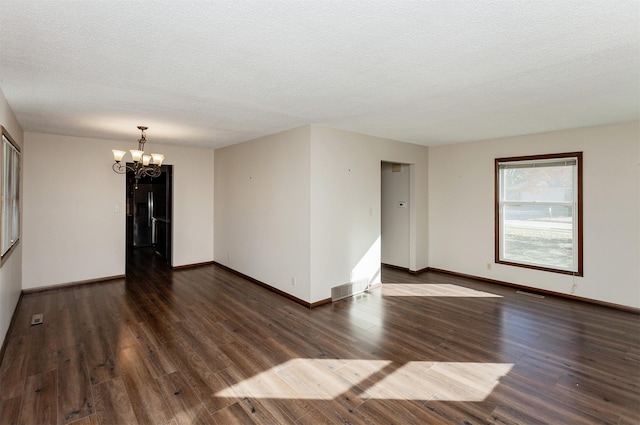 spare room with dark wood-type flooring, an inviting chandelier, and a textured ceiling