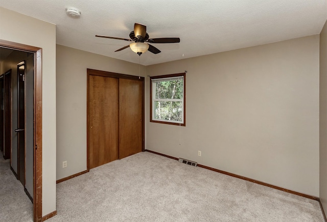 unfurnished bedroom featuring ceiling fan, light colored carpet, a textured ceiling, and a closet