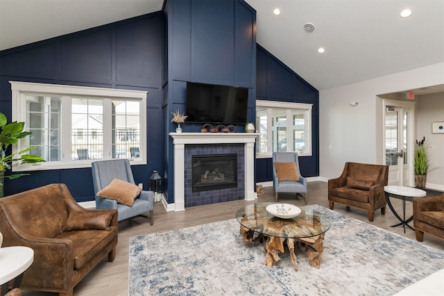 living room featuring high vaulted ceiling, light hardwood / wood-style flooring, a healthy amount of sunlight, and a tiled fireplace