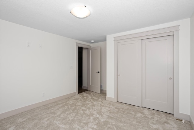 unfurnished bedroom featuring a closet, light colored carpet, a textured ceiling, and baseboards