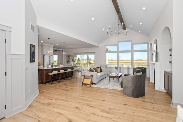 living room with light hardwood / wood-style floors, a notable chandelier, beam ceiling, and a towering ceiling