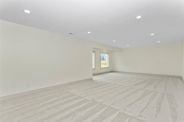 empty room featuring light carpet, baseboards, a textured ceiling, and recessed lighting