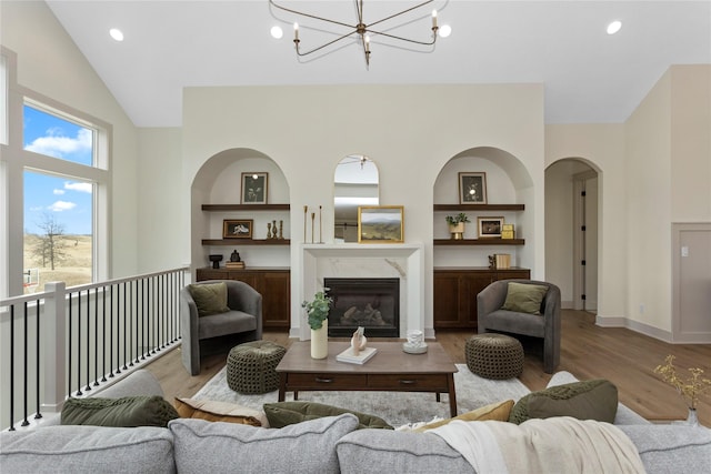 living room with a notable chandelier, wood finished floors, a high end fireplace, baseboards, and built in features