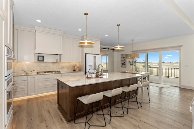 kitchen with tasteful backsplash, a kitchen island with sink, a sink, white cabinetry, and white appliances