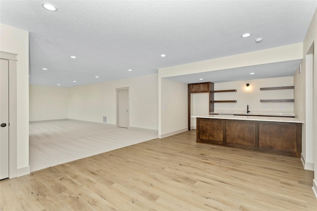 unfurnished living room featuring light wood-style flooring, baseboards, a textured ceiling, and recessed lighting