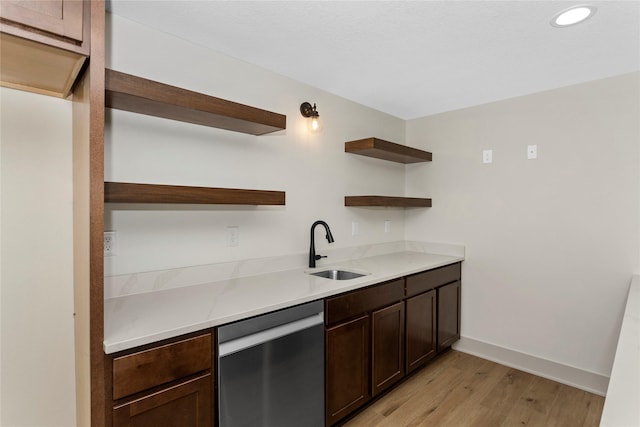 kitchen with dark brown cabinetry, stainless steel dishwasher, light wood-style floors, open shelves, and a sink