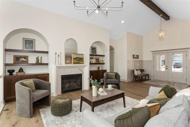 living area with a premium fireplace, light wood-type flooring, built in shelves, a chandelier, and beam ceiling