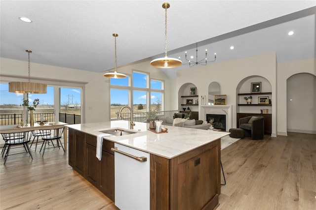 kitchen featuring light wood finished floors, an island with sink, white dishwasher, built in shelves, and a sink