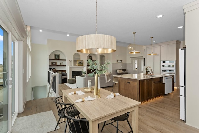 dining room with recessed lighting, a fireplace, built in shelves, and light wood-style floors