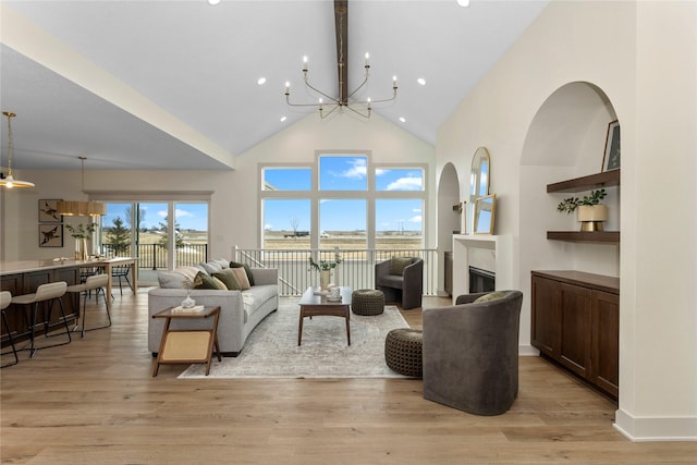 living room featuring baseboards, a glass covered fireplace, light wood-style flooring, high vaulted ceiling, and a notable chandelier