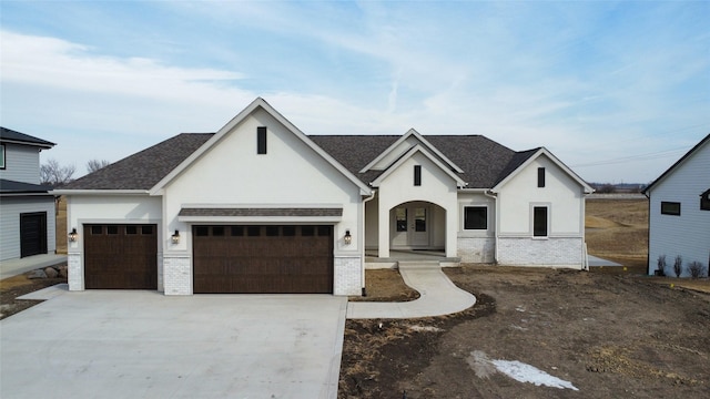 view of front of property featuring a garage, driveway, brick siding, and stucco siding