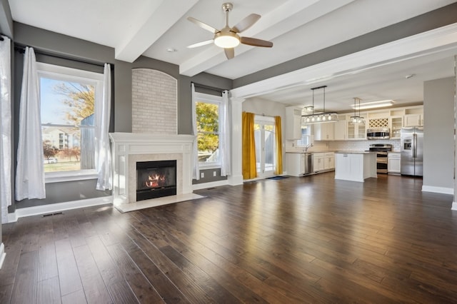 unfurnished living room featuring beamed ceiling, ceiling fan, a healthy amount of sunlight, and dark hardwood / wood-style flooring