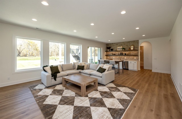 living area with light wood-style flooring, arched walkways, baseboards, and recessed lighting