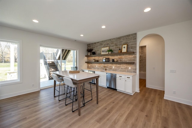 kitchen featuring white cabinetry, light countertops, stainless steel dishwasher, backsplash, and a kitchen bar