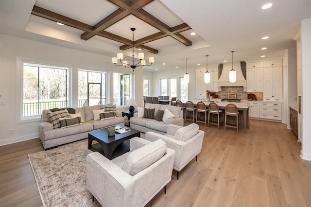 living area with coffered ceiling, plenty of natural light, a notable chandelier, and light wood finished floors