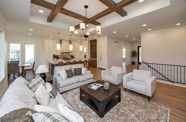 living room with a wealth of natural light, coffered ceiling, an inviting chandelier, and wood finished floors