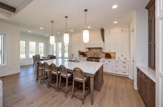 kitchen with decorative backsplash, stove, light wood-type flooring, premium range hood, and a sink