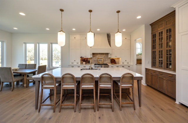 kitchen featuring decorative backsplash, a spacious island, glass insert cabinets, a breakfast bar, and premium range hood