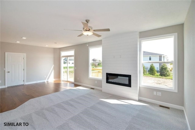 unfurnished living room featuring a large fireplace, light hardwood / wood-style floors, a healthy amount of sunlight, and ceiling fan