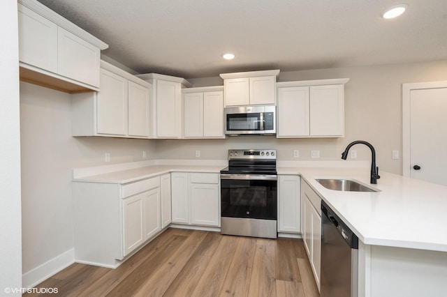 kitchen with appliances with stainless steel finishes, light hardwood / wood-style floors, sink, and white cabinets