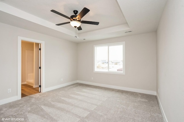 carpeted spare room with ceiling fan and a raised ceiling