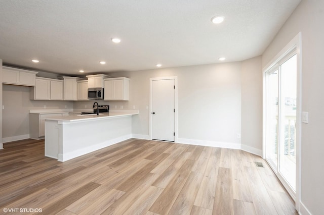 kitchen with appliances with stainless steel finishes, white cabinetry, sink, kitchen peninsula, and light hardwood / wood-style flooring