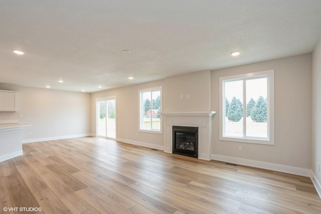 unfurnished living room with a healthy amount of sunlight, a textured ceiling, and light hardwood / wood-style floors