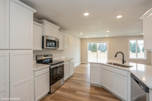 kitchen featuring sink, white cabinetry, a textured ceiling, stainless steel appliances, and light hardwood / wood-style floors