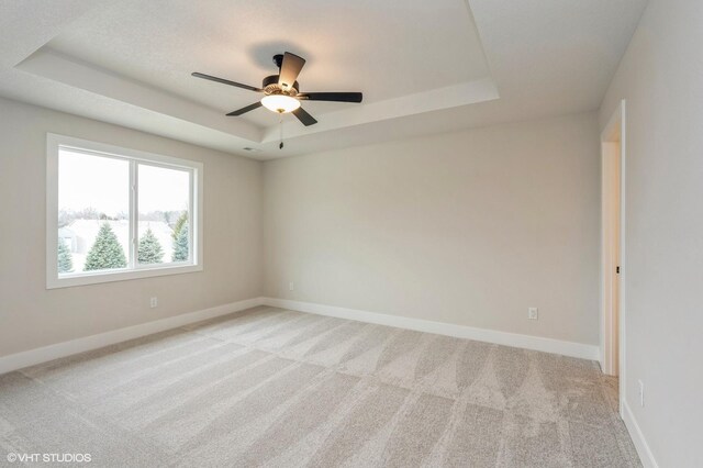 empty room featuring light carpet, ceiling fan, and a tray ceiling