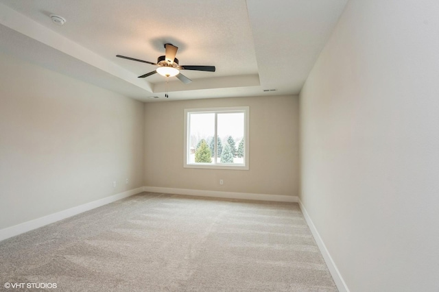 carpeted empty room featuring ceiling fan and a raised ceiling