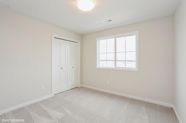 unfurnished bedroom with light colored carpet and a closet