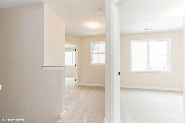 corridor with light carpet and a textured ceiling